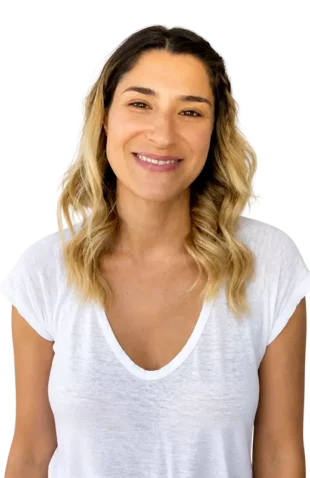 Smiling person with wavy blonde hair wearing a white t-shirt against a plain background.